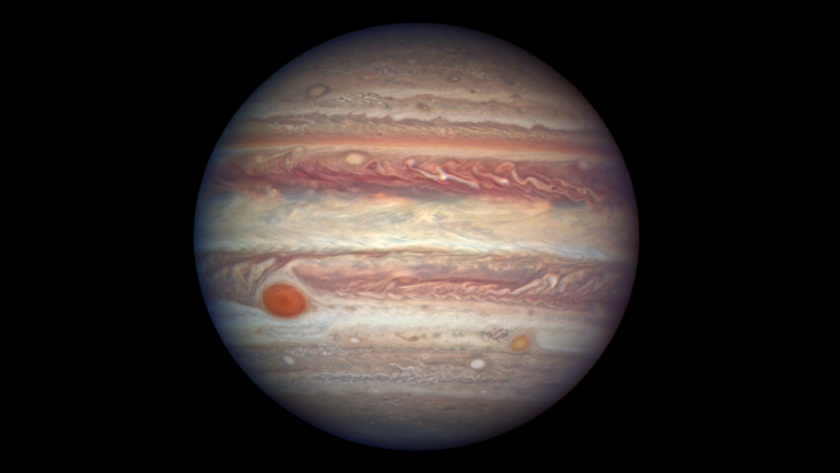 High-resolution telescopic view of Jupiter at opposition showing cloud bands, the Great Red Spot, and its four Galilean moons visible nearby.